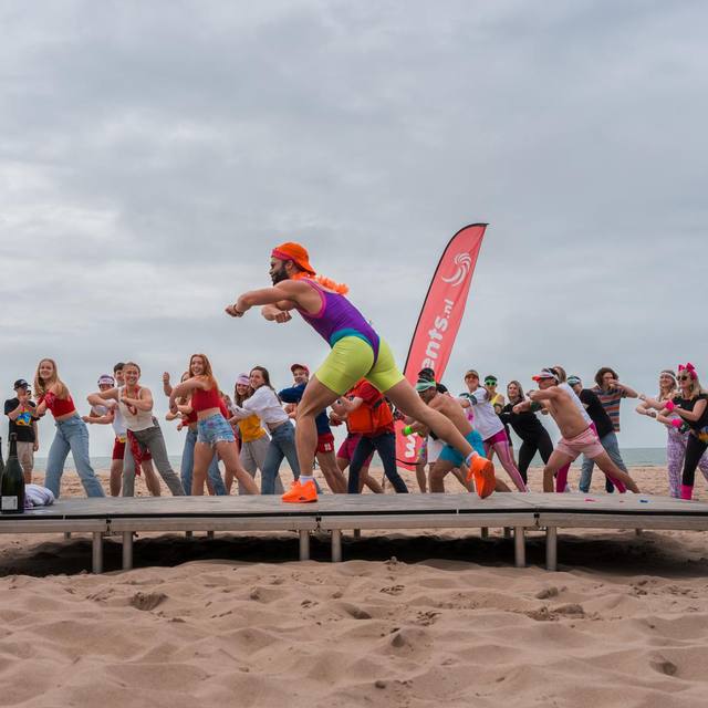 Instructor on a beach stage, crowd following the move